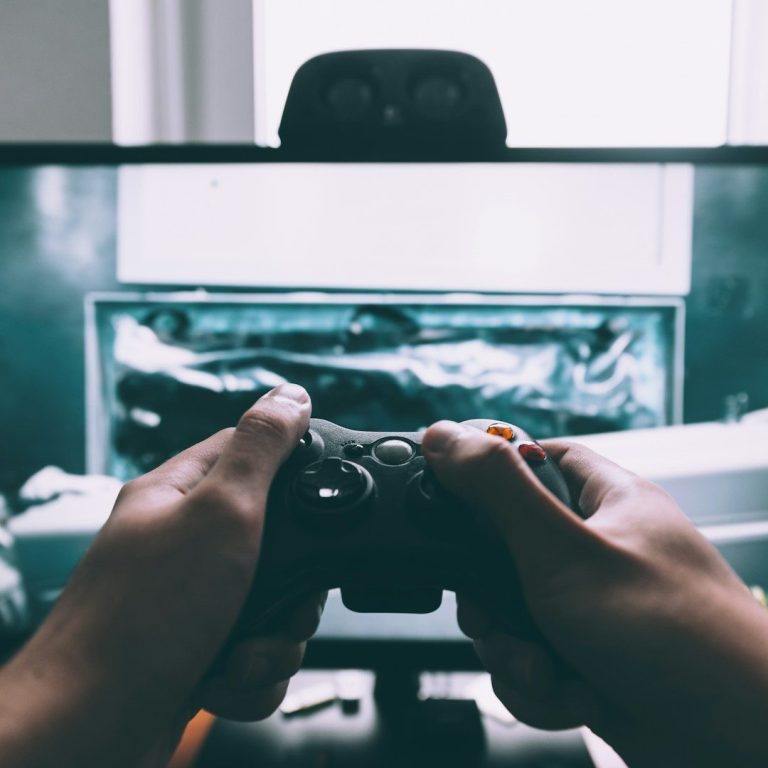 Hands holding a gaming controller in front of a computer screen.